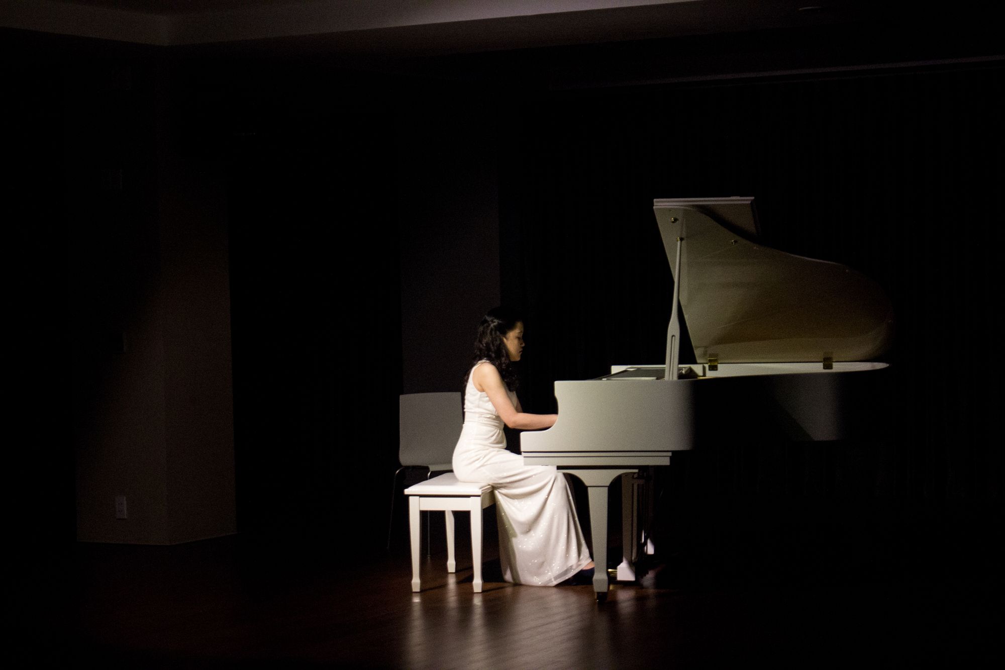 A classical pianist performing at a grand piano under stage light