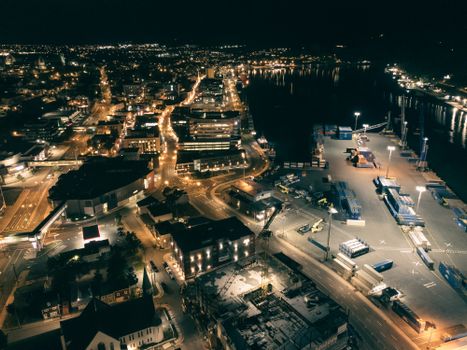 A stunning aerial view of a vibrant coastal city at night, showcasing city lights and a bustling port.