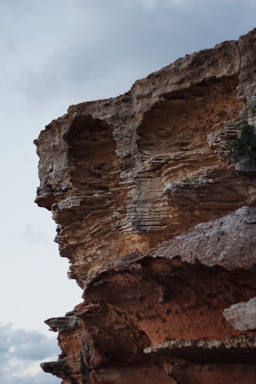 Free A close-up view of an eroded rock formation with layered textures under an overcast sky. Stock Photo