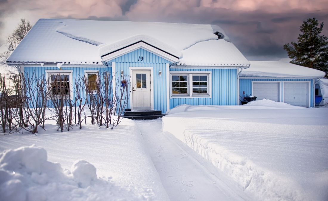 Blue house covered in snow during winter with a serene sky backdrop