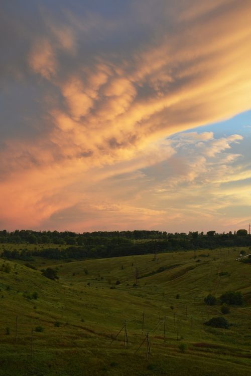 Free A serene sunset over lush green rural landscape with dramatic clouds. Stock Photo