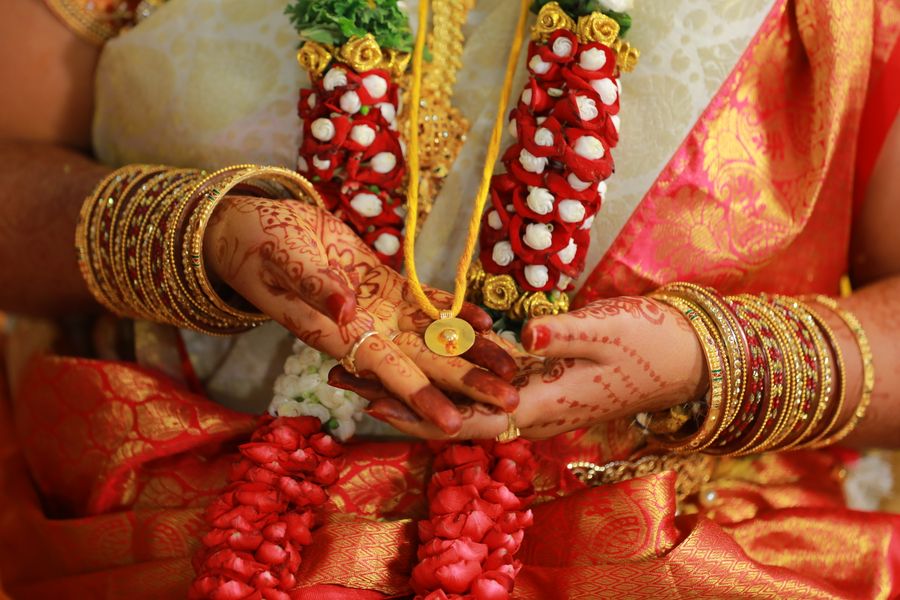 Hands holding the thaali with red garlands and gold coins