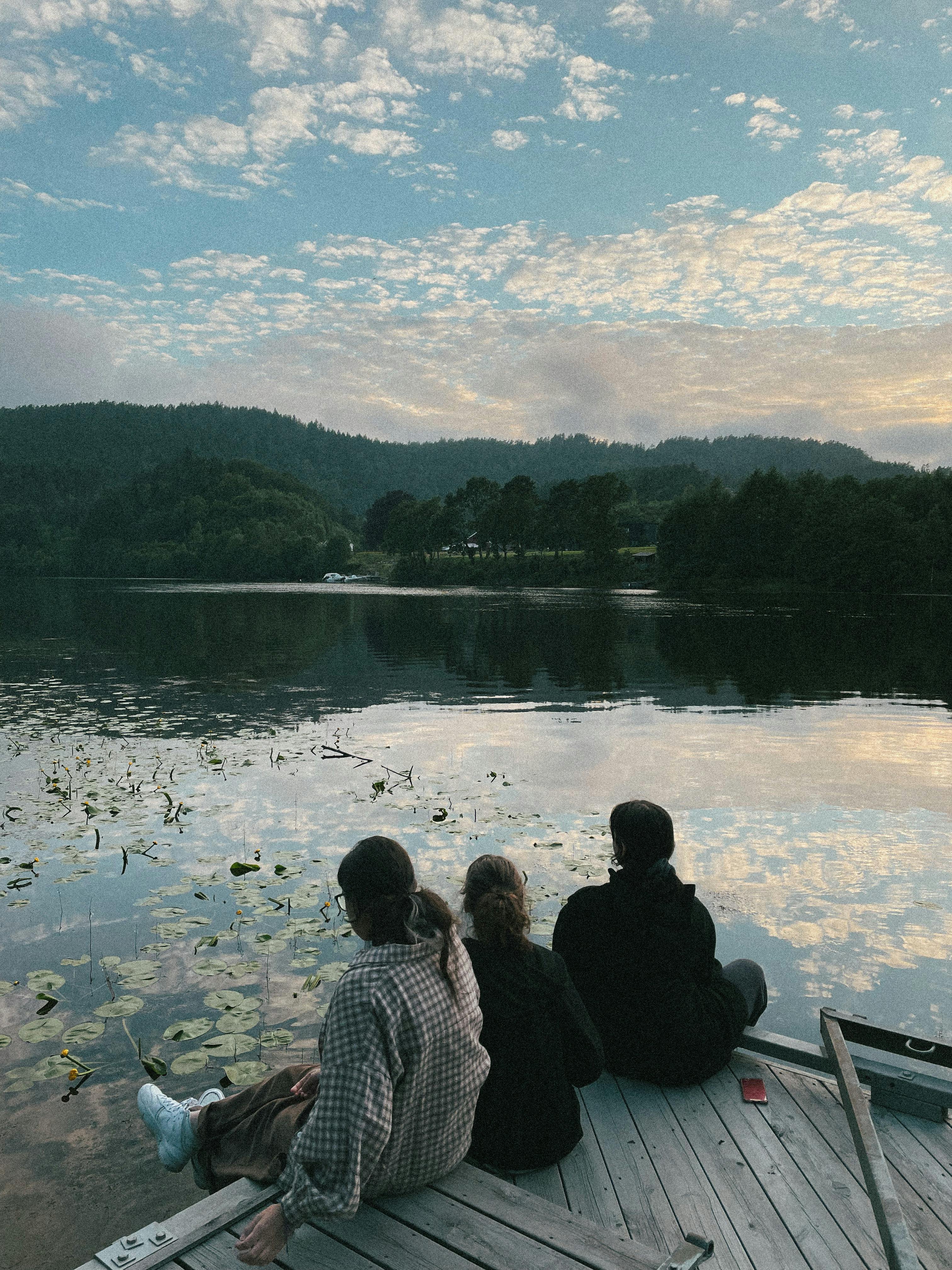 Three people enjoying peaceful reflection by a serene lake, surrounded by nature.