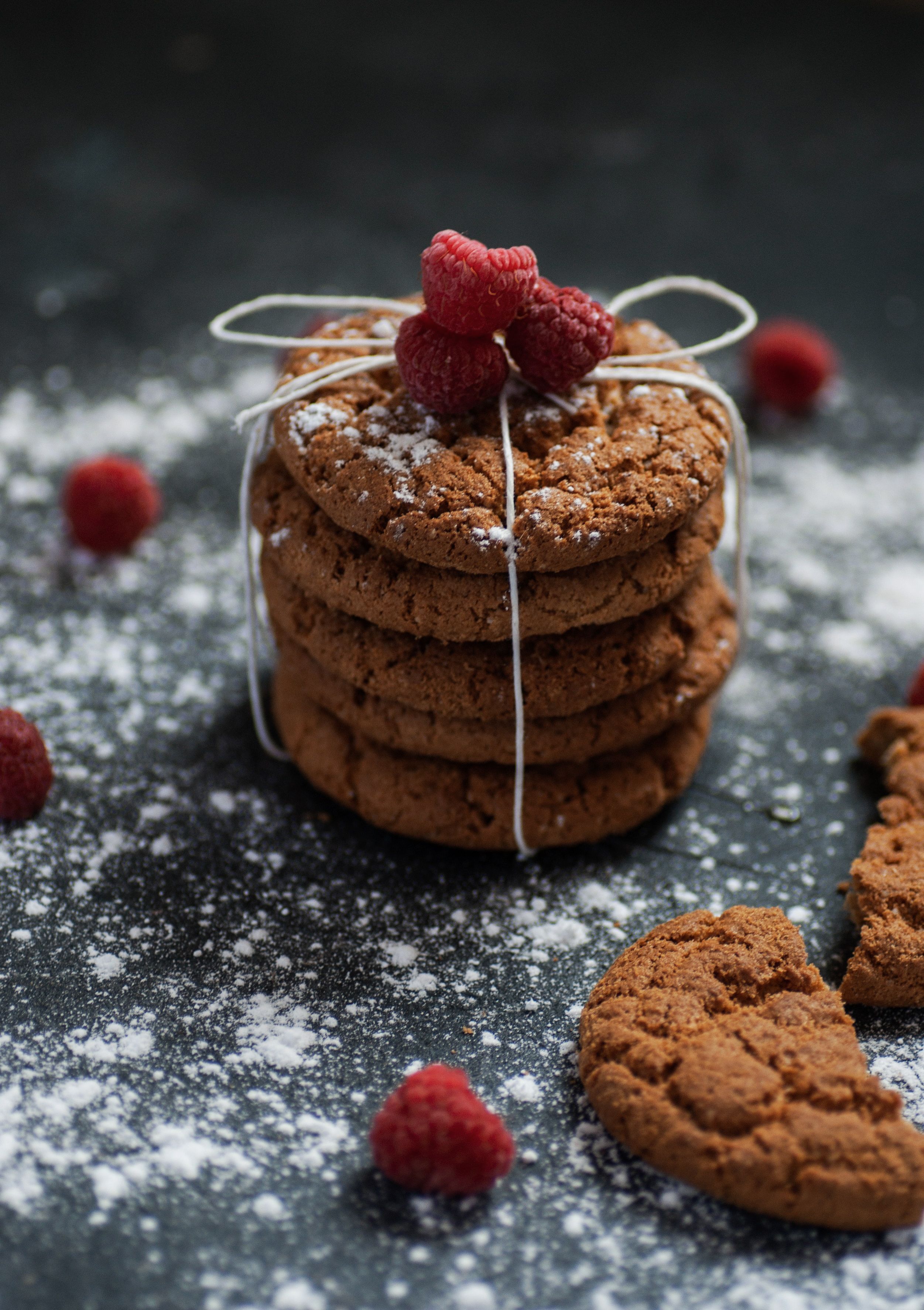 Stack of chocolate cookies topped with raspberries and dusted with powdered sugar on a dark background.