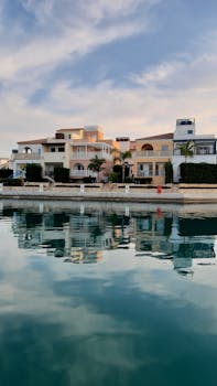 Scenic view of elegant waterfront homes mirrored in a calm canal under a serene sky.
