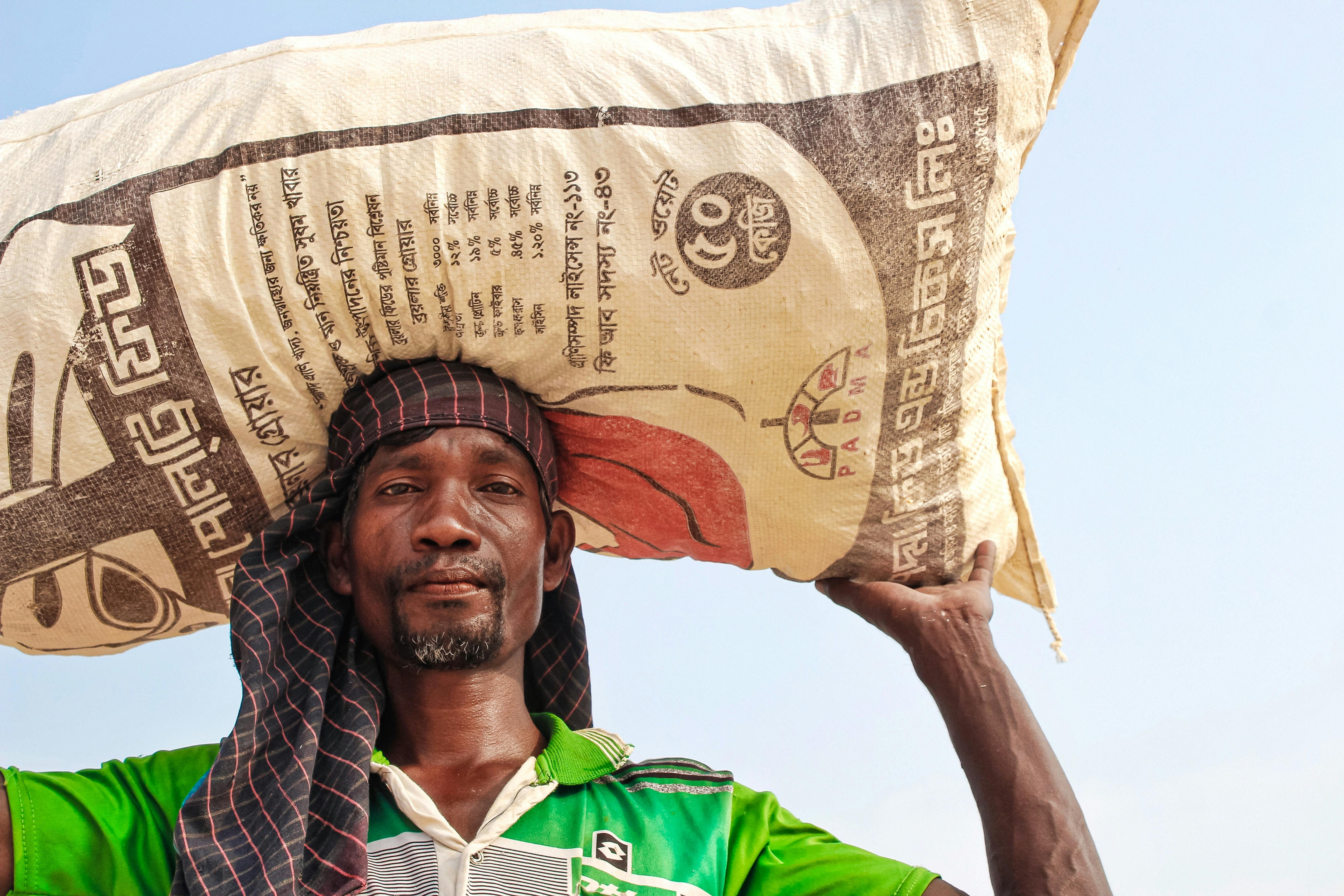 Man Carrying Sack Near White Wall · Free Stock Photo