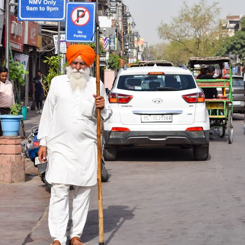 Elderly Man Wearing an Orange Turban Standing on the Street with a Sign No Parking in a Hand