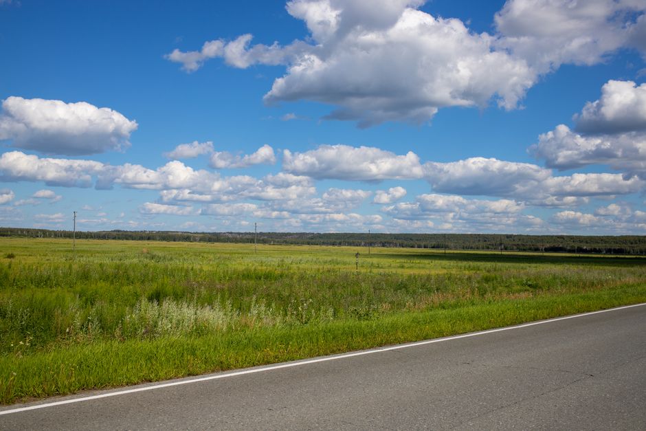 Breathtaking view of a rural road beside vast green fields under a vibrant blue sky filled with clouds.