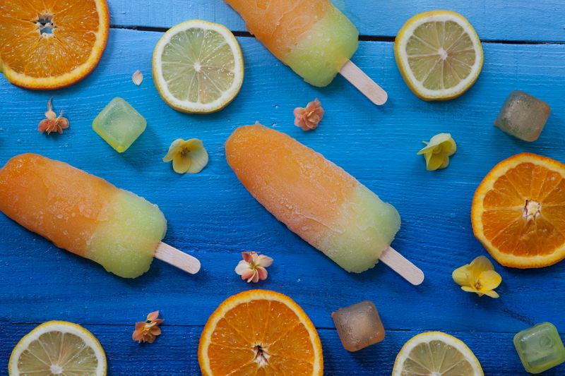 Colorful citrus ice pops with slices of lemon and orange on a blue surface