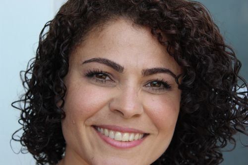 Free Close-up of a happy woman with curly hair, smiling genuinely outdoors. Stock Photo