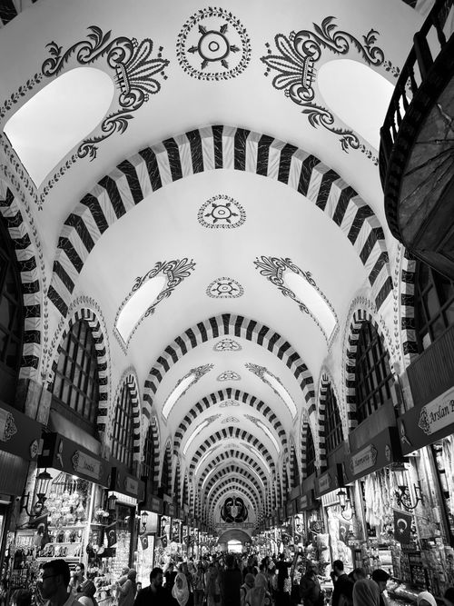 Free Monochrome view of bustling shoppers under ornate arches in a traditional Middle Eastern bazaar. Stock Photo