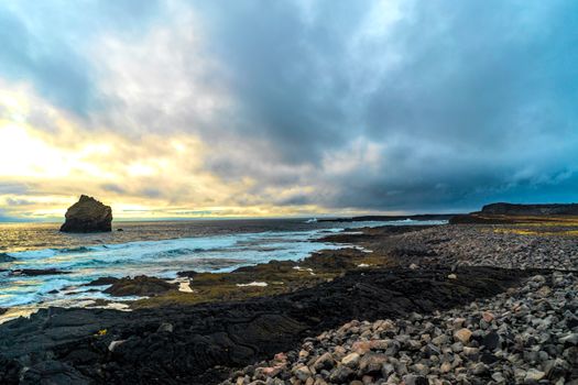 Stunning rocky seashore at sunset with dramatic clouds and ocean waves crashing.