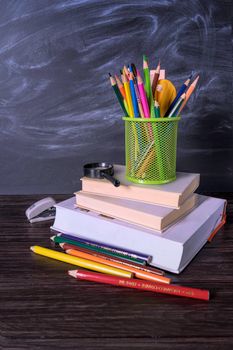 Pile of books and stationery on a desk with a chalkboard backdrop, ideal for educational themes.