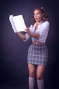 A Woman in White Shirt and Gray Plaid Skirt Holding a Book