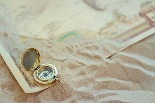 A close-up of a vintage compass on sand with a map, symbolizing travel and exploration.