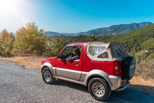 A red SUV driving through the mountainous landscape of Alanya, Turkey on a sunny day.