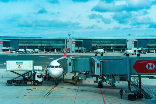 Free Airplane at gate with jetway and loading trucks at a bustling airport. Stock Photo