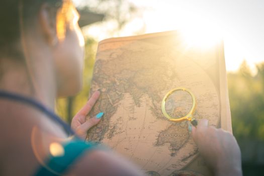 A person examines a world map using a magnifying glass outdoors in bright sunlight, capturing a sense of exploration.