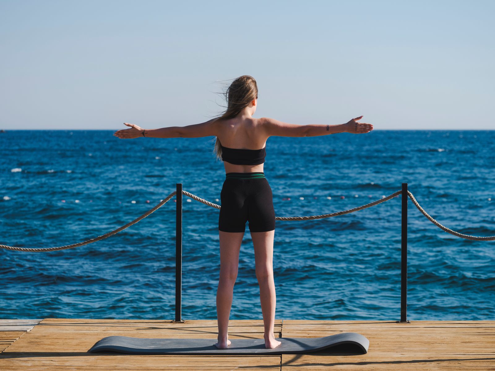 Woman standing on a dock with arms outstretched in a heart-opening yoga stretch facing the ocean