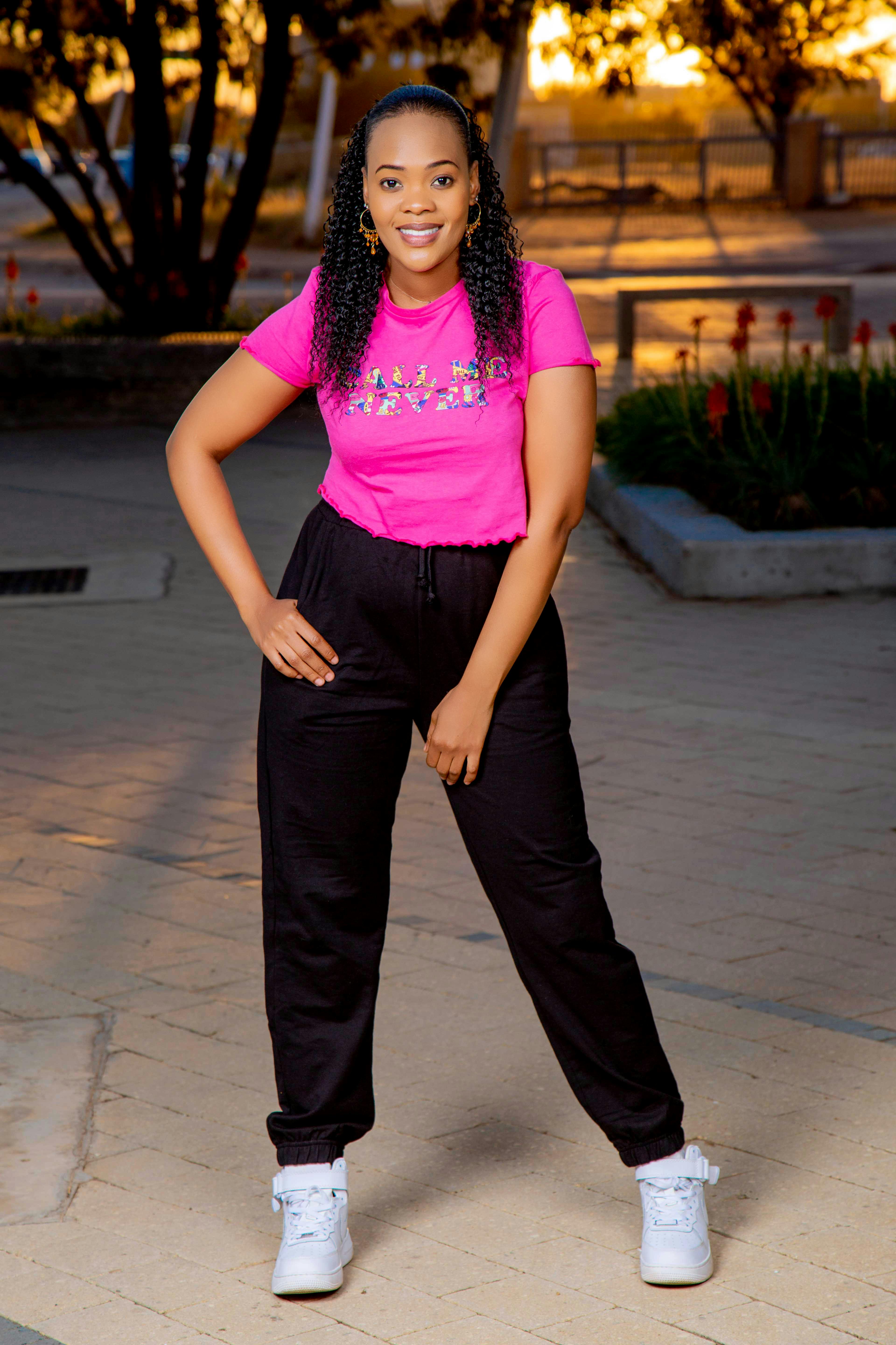 Smiling young woman in casual attire poses outdoors during sunset.