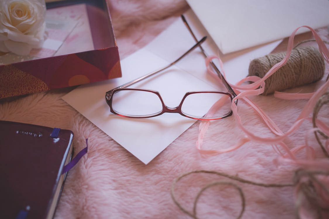 Free Eyeglasses Beside Pink Yarn on Pink Bed Blanket Stock Photo