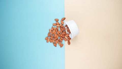 A bowl of almonds spills onto a blue and beige backdrop. Minimalist food concept.