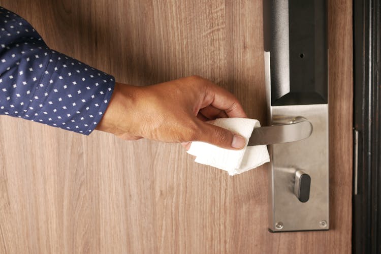 Person Holding A Metal Door Handle Using White Tissue Paper