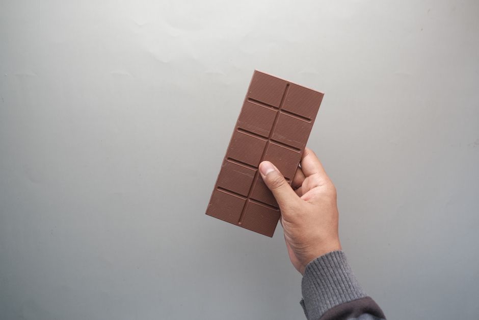 Hand holding a chocolate bar against a gray background, perfect for dessert and confectionery themes.