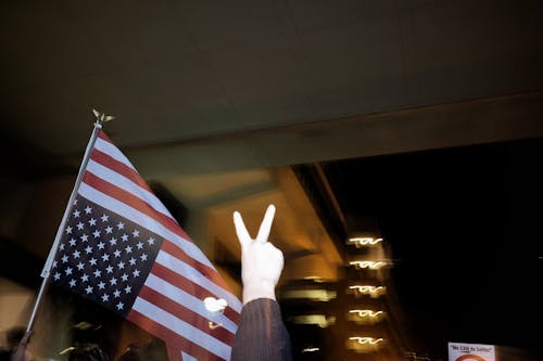 A Person Making a Peace Sign beside an Upside Down American Flag