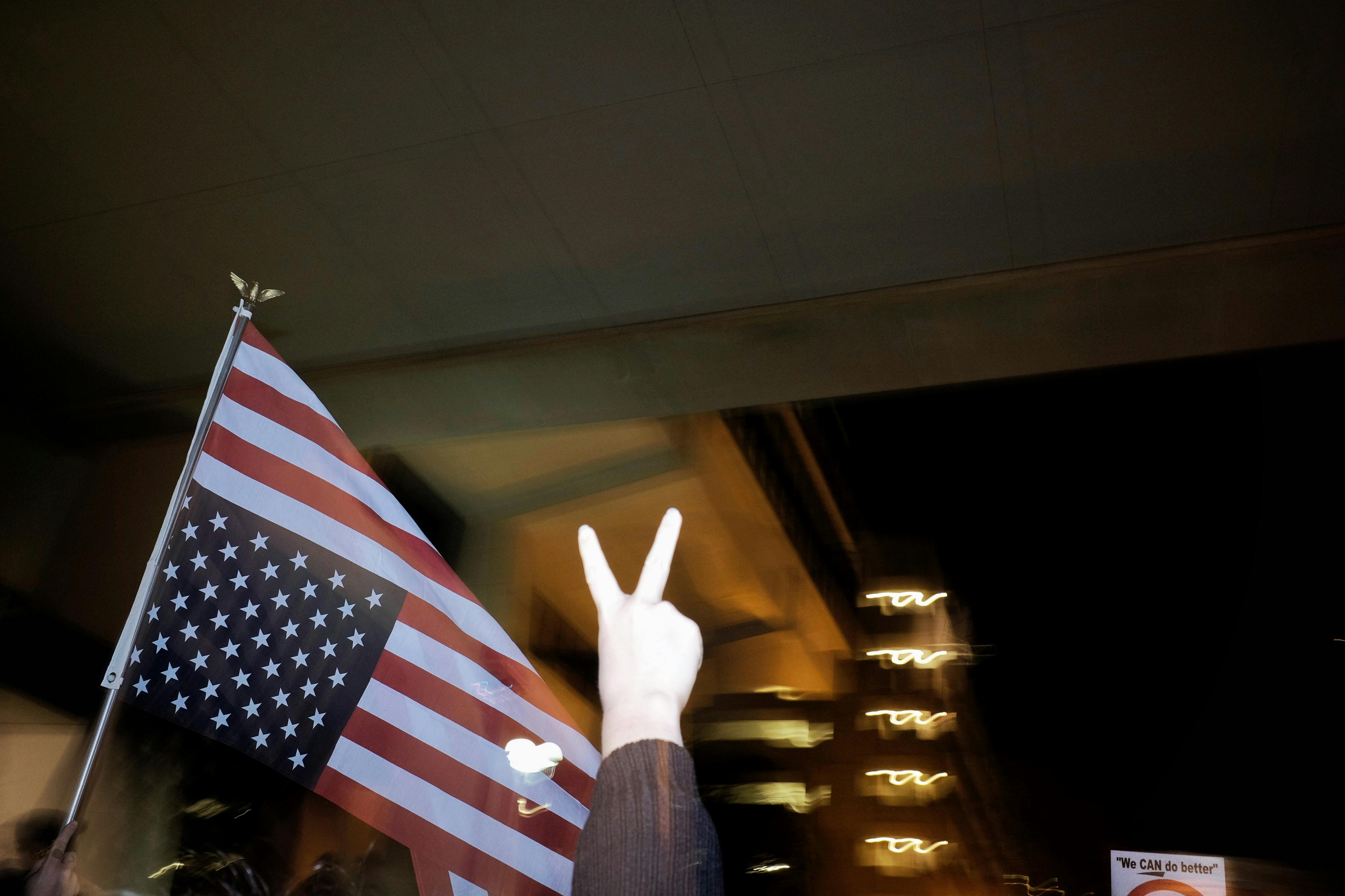 A Person Making a Peace Sign beside an Upside Down American Flag · Free