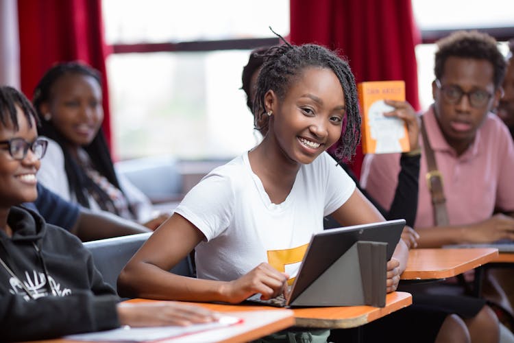 Young Girl Smiling In White Shirt Holding An IPad Inside A Classroom