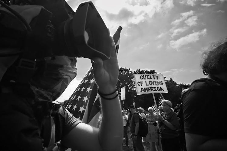 A Grayscale Photo Of A Person Filming A Protest