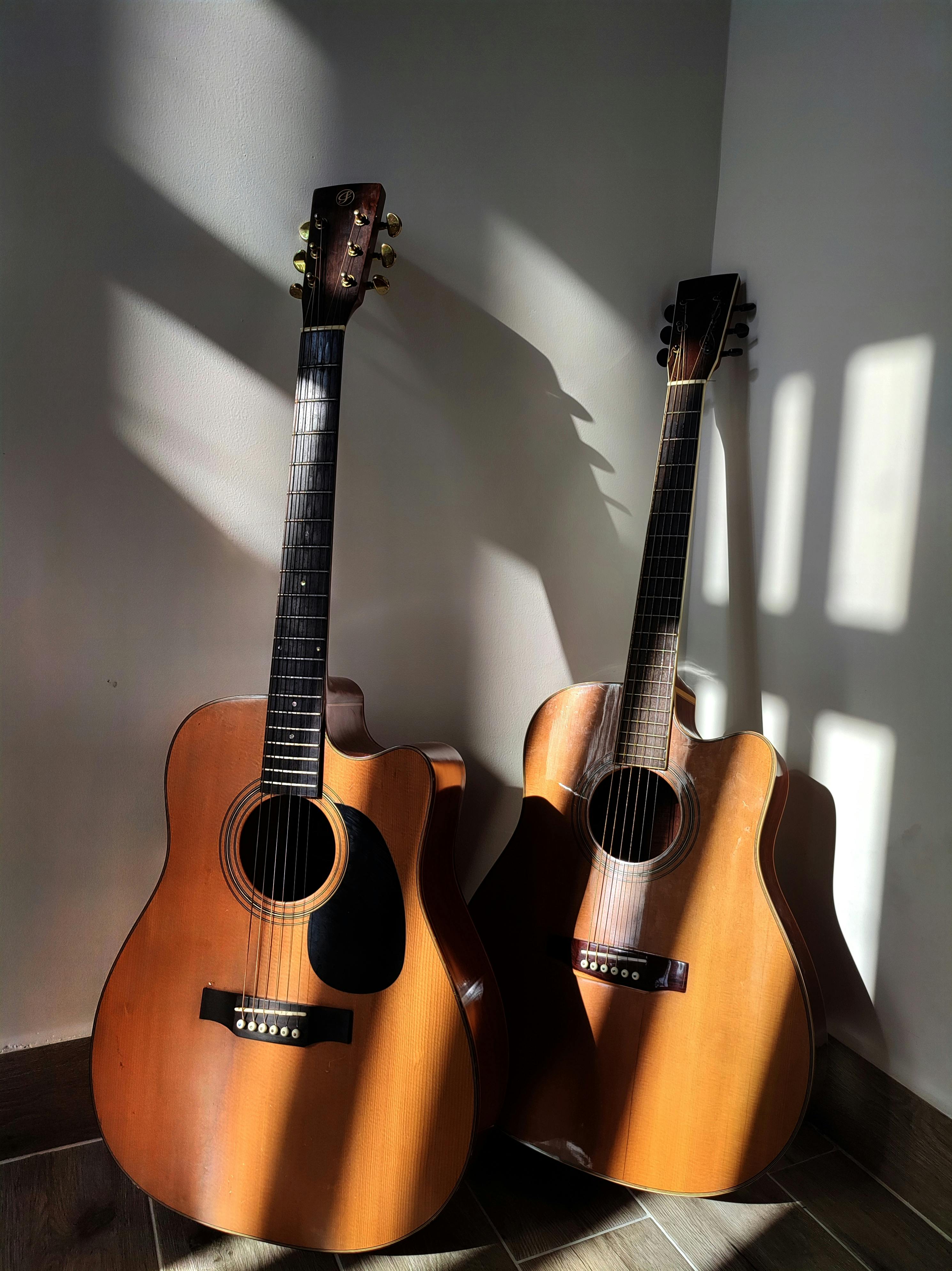 Free Two classic wooden acoustic guitars with shadows on a wall, creating a vintage vibe. Stock Photo
