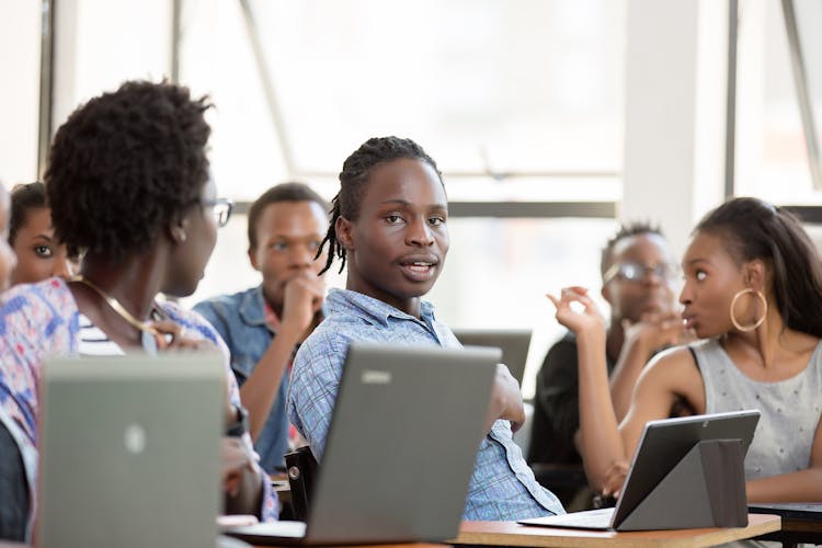 Young People Sitting In A Classroom With Laptops And Tablets 