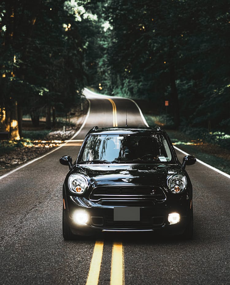 Black Car Driving Down A Road Lines By Trees