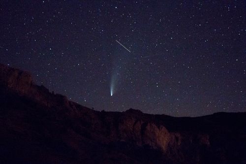 Free Stunning view of a star-filled night sky with a brilliant comet streaking above rocky mountains. Stock Photo