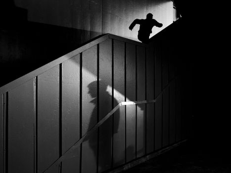 Dynamic black and white silhouette of a man running upstairs with dramatic shadows.