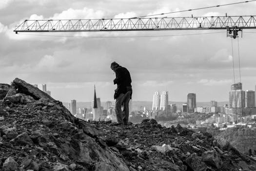 Silhouette of a man standing on a rocky hill with urban skyline in the background.