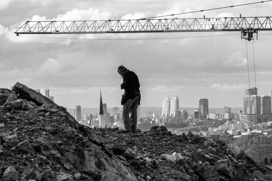 Silhouette of a man standing on a rocky hill with urban skyline in the background.