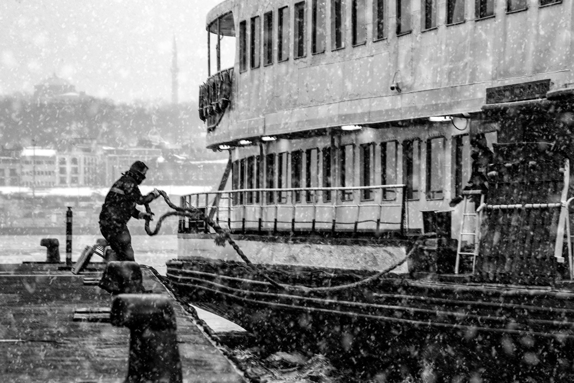 A person docks a ship amidst a snowstorm in a black and white scene.