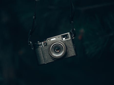 Close-up of a vintage black camera hanging by strap in a shadowy forest setting.