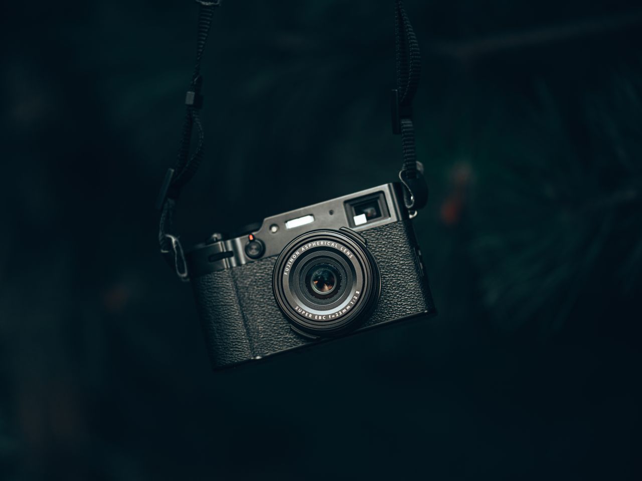 close up of a vintage black camera hanging by strap in a shadowy fores