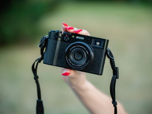 Free A hand holding a vintage-style camera outdoors, with red-painted nails. Perfect for photography themes. Stock Photo