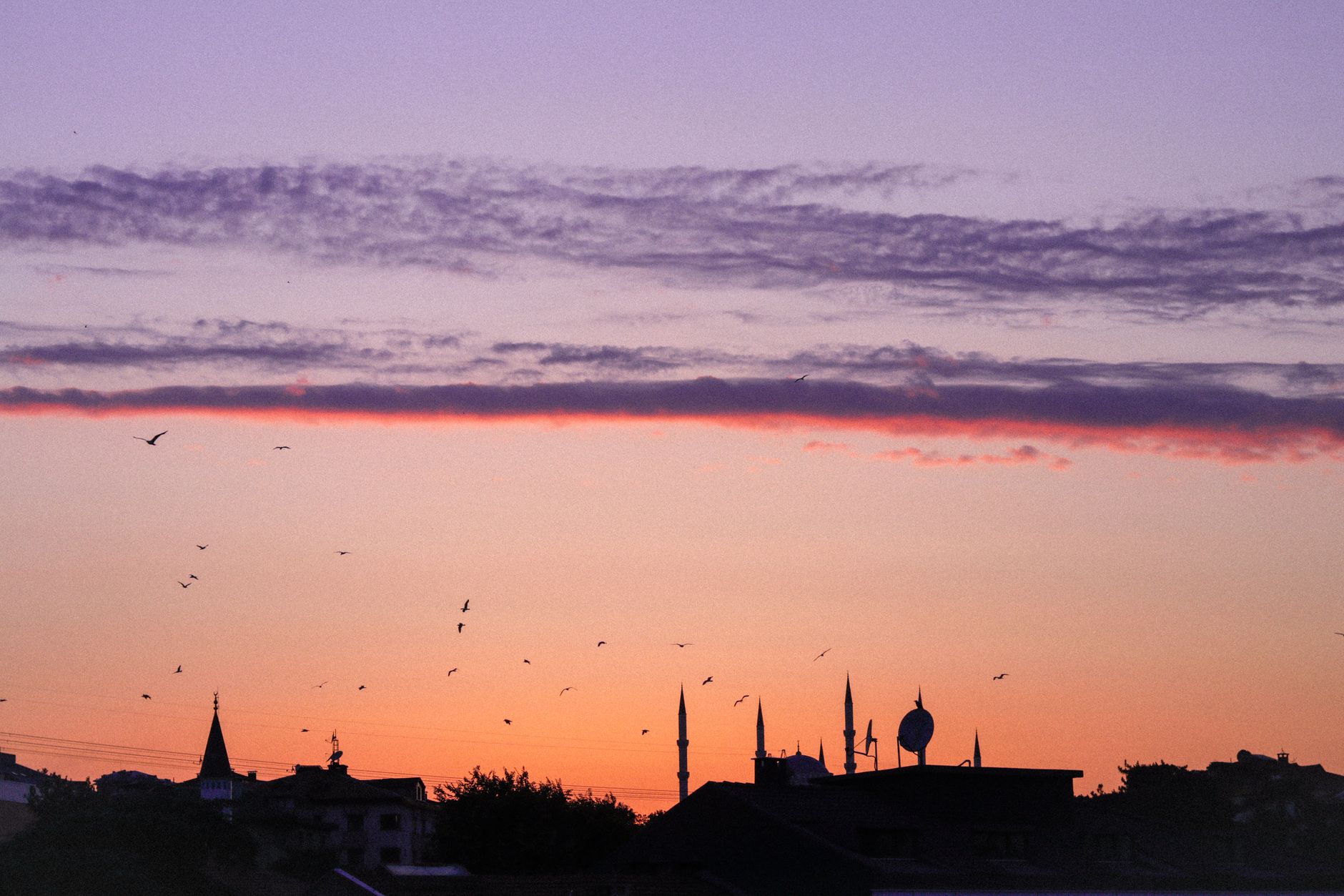 Silhouette of city skyline with minarets against a colorful sunrise sky.