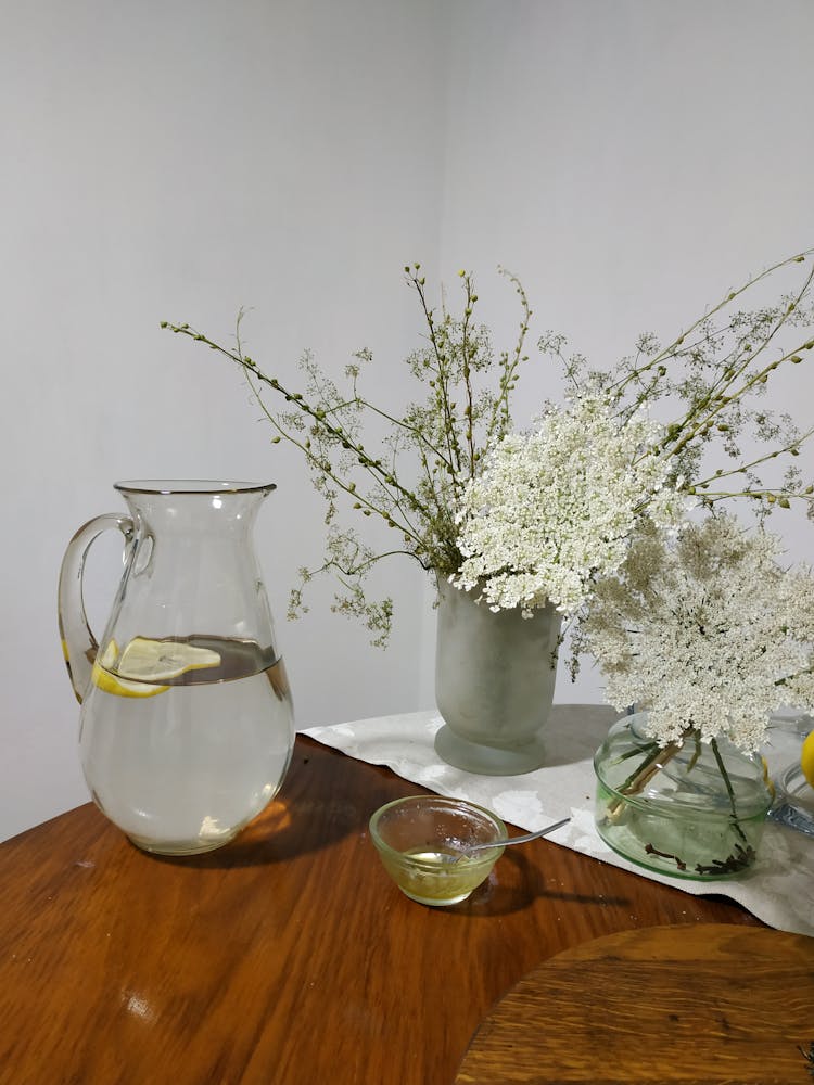 WA Pitcher Of Lemon Water Beside White Flowers In Clear Vase