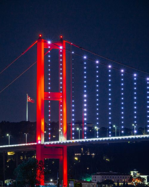 Free Illuminated Bosphorus Bridge with city lights and Turkish flag at night in Istanbul. Stock Photo