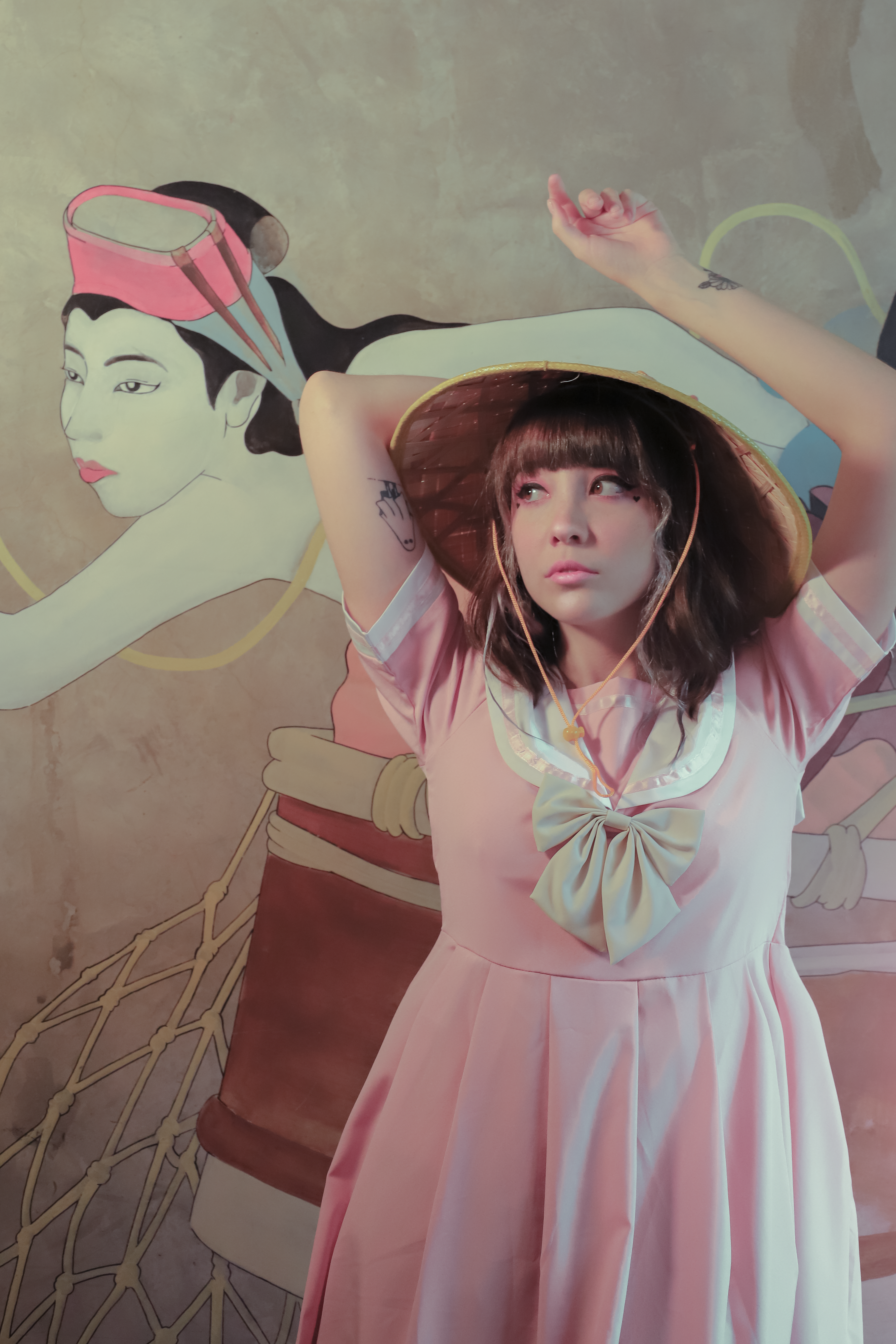 Fashionable woman in pink dress with hat posing indoors by mural art.