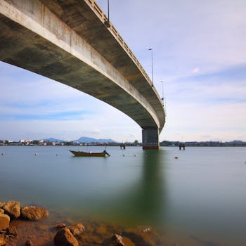 一座风景如画的现代桥梁横跨在宁静的河流上，桥下有一艘小船，凸显了建筑设计与宁静环境的和谐