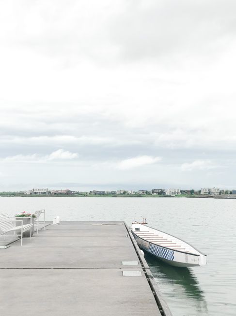 Tranquil scene of an empty dock with a single boat on a calm lake under cloudy skies.