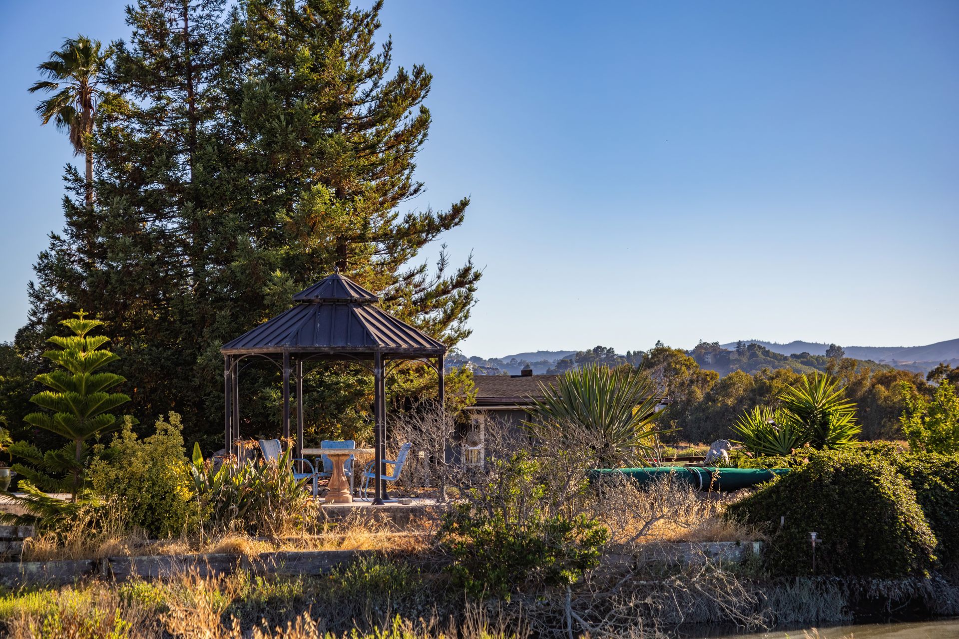 A peaceful garden gazebo surrounded by lush trees and scenic views under a clear sky.
